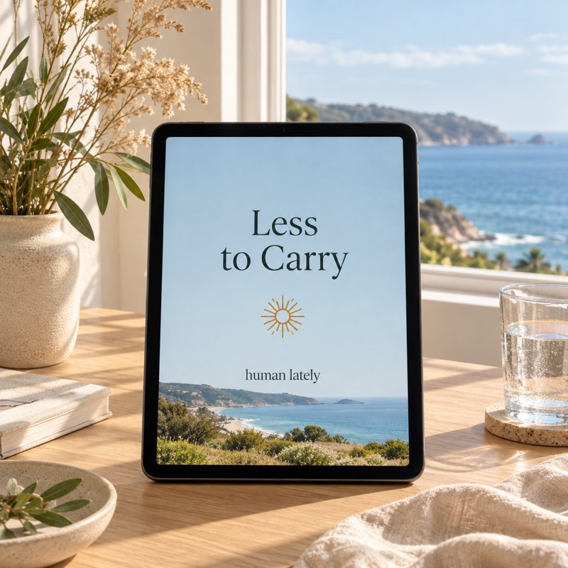 A tablet with a sky-blue Less to Carry cover by a window overlooking the coast, with a glass of water and linen