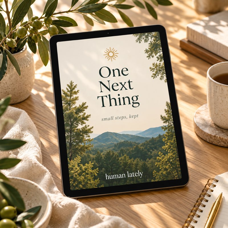 A tablet with a forest-green One Next Thing cover on a sunlit oak desk, with olive leaves and linen